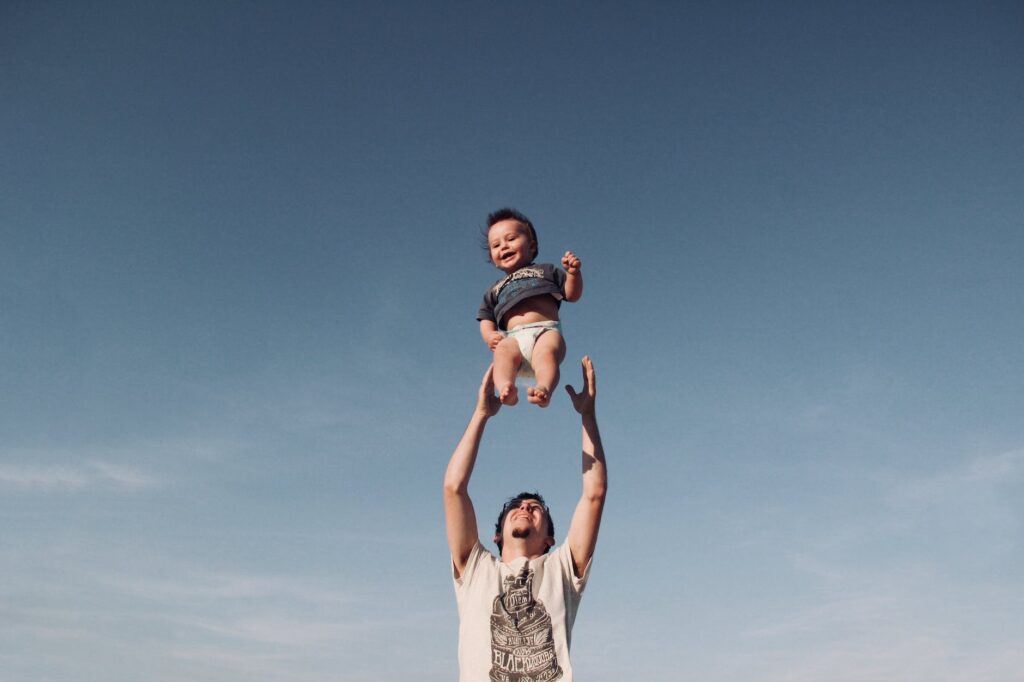 photo of a man raising baby under blue sky