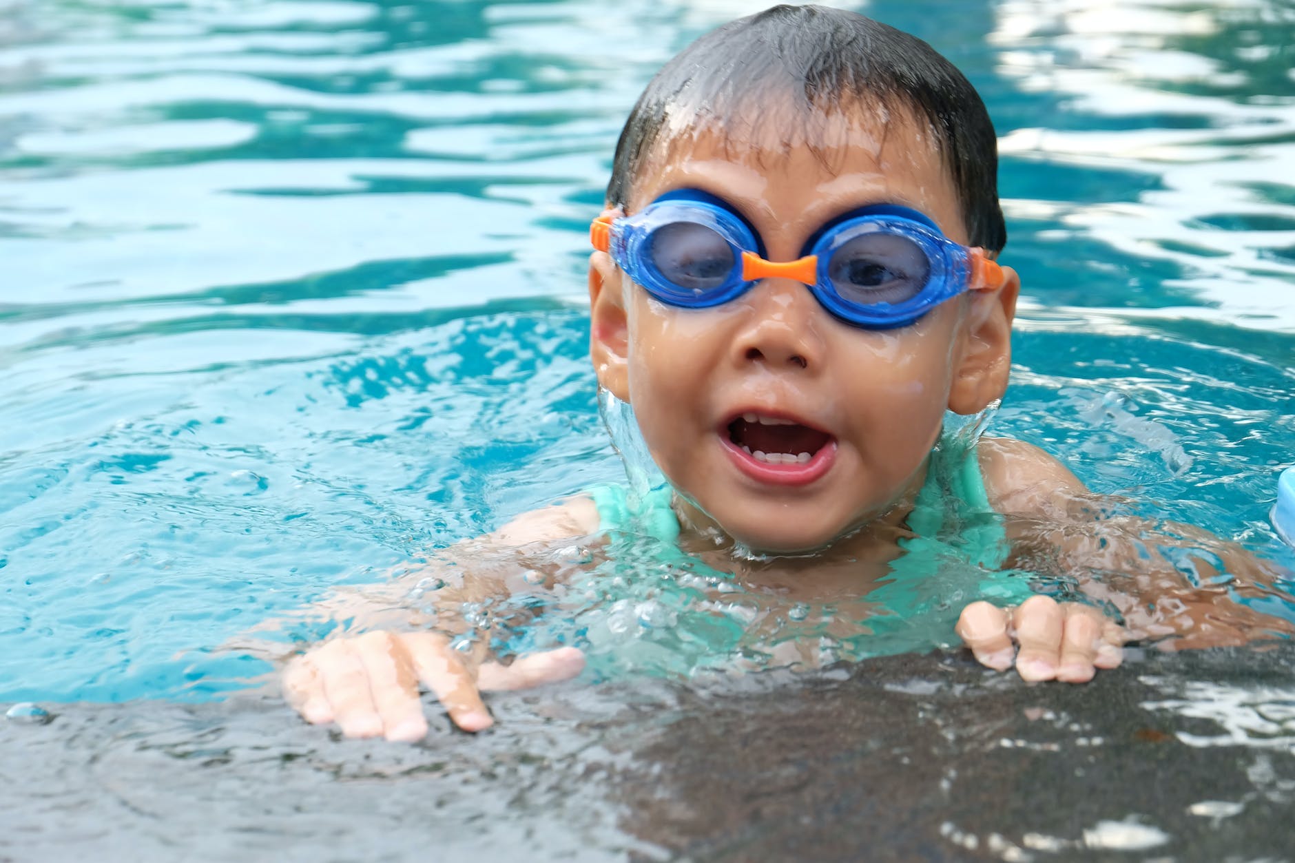 toddler swimming on pool wearing blue goggles