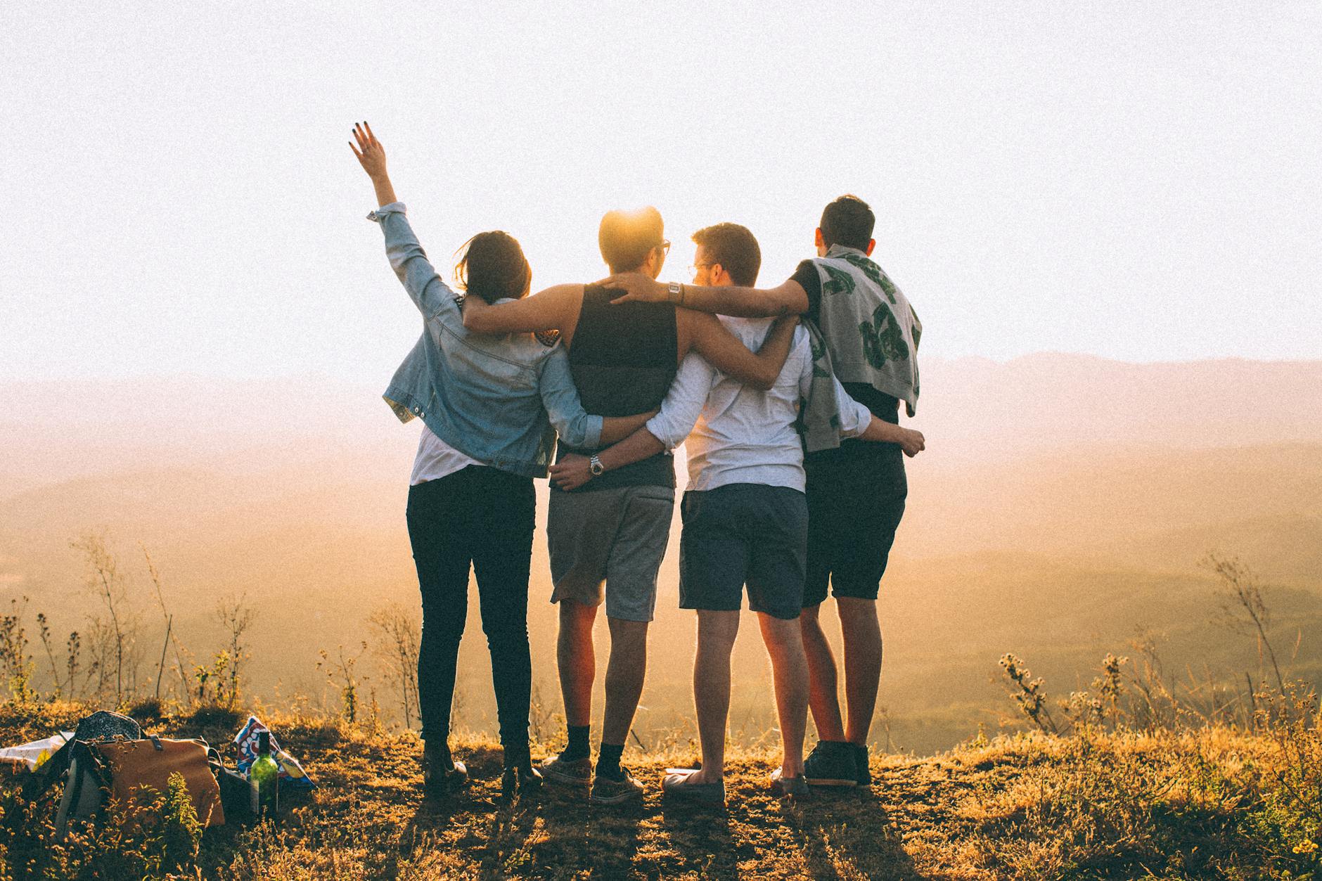 anonymous friends standing together at sunset in mountains