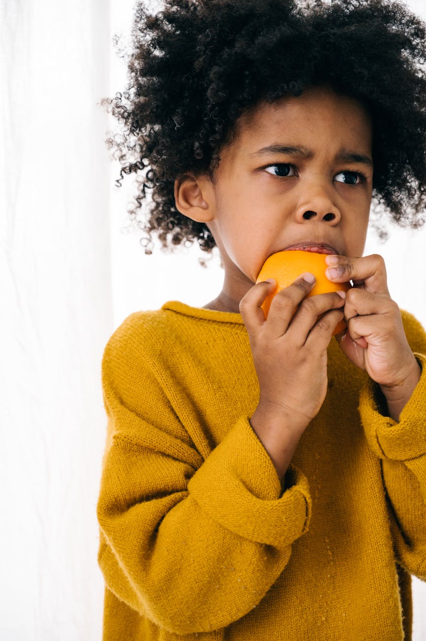 funny ethnic kid biting sweet orange on white background