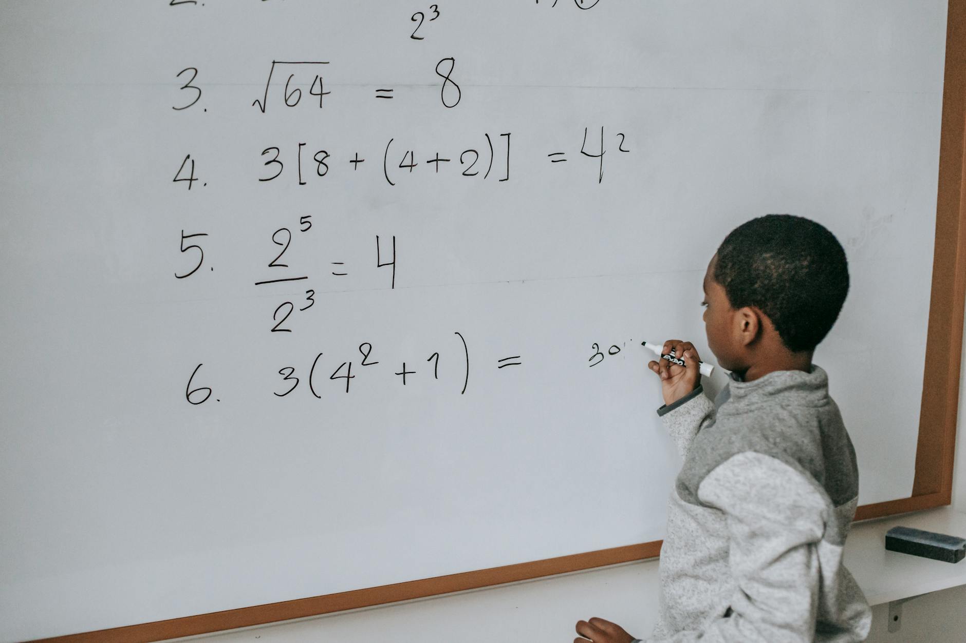 black schoolboy solving math examples on whiteboard in classroom