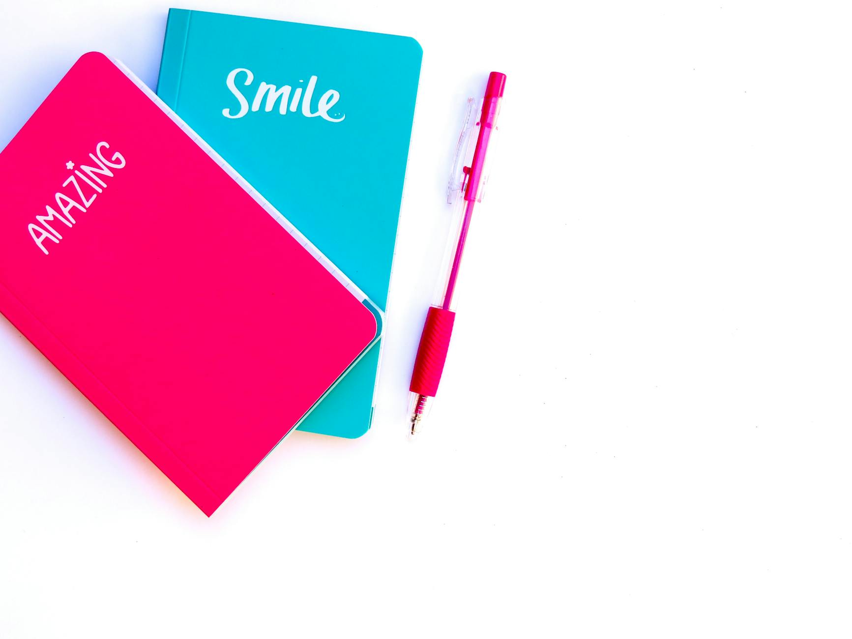 pink and blue notebooks beside red click pen