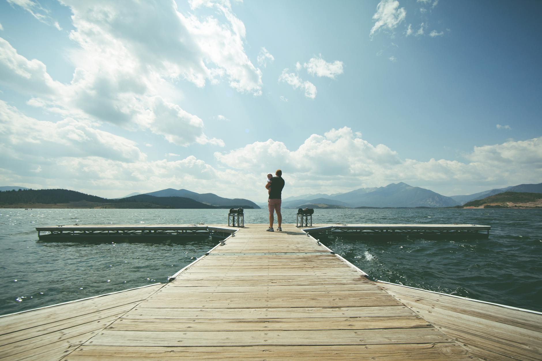 person standing on brown wooden dock under clue sky during daytime