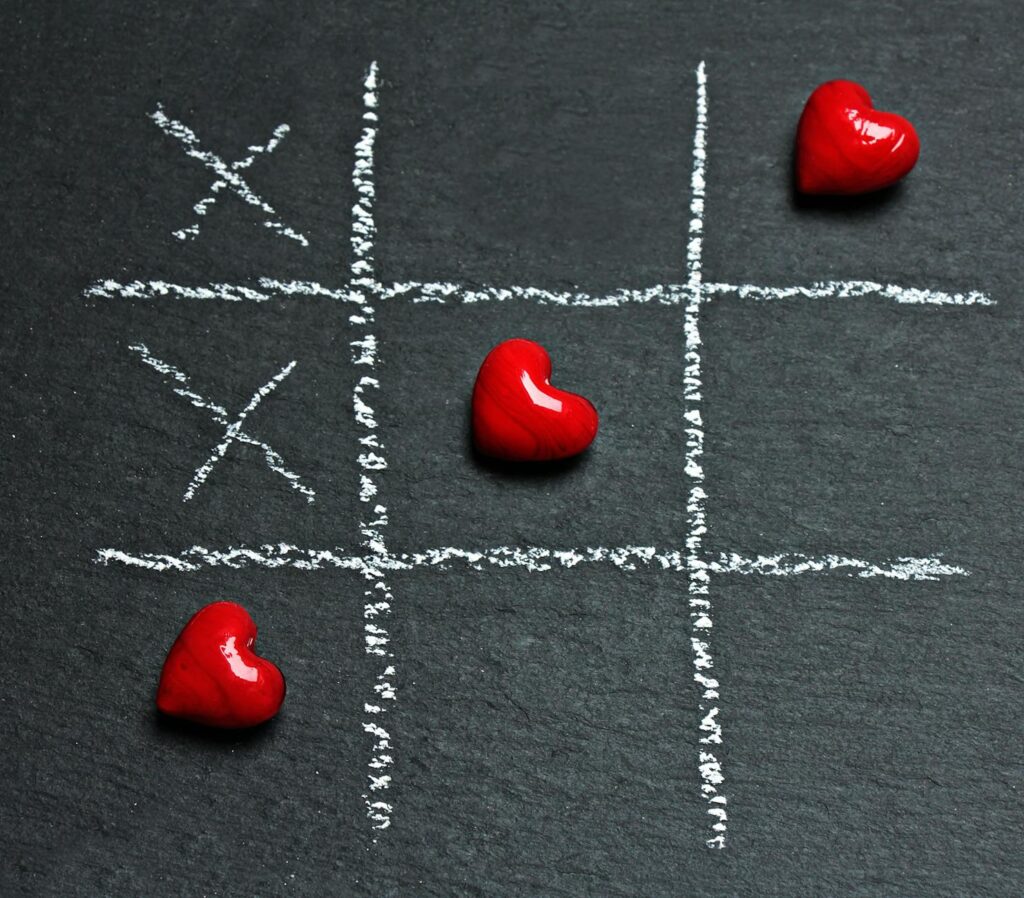 three heart shaped red stones placed on tic tac toe game bord