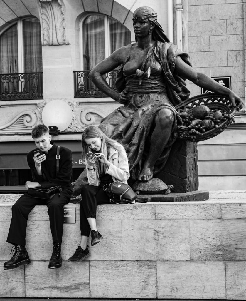 young people next to parisian statue using phones