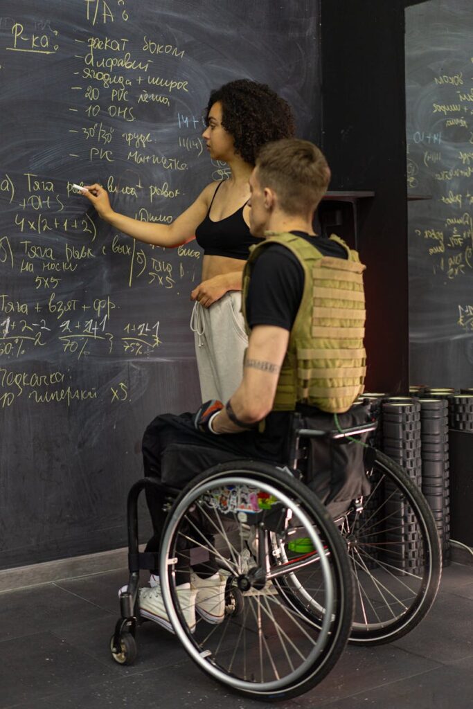 a man sitting on a wheelchair while listening to the woman writing on the board