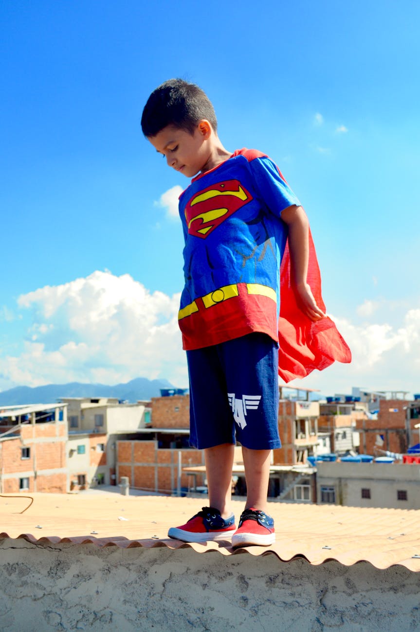 photo of a little boy in a superman costume standing on a roof