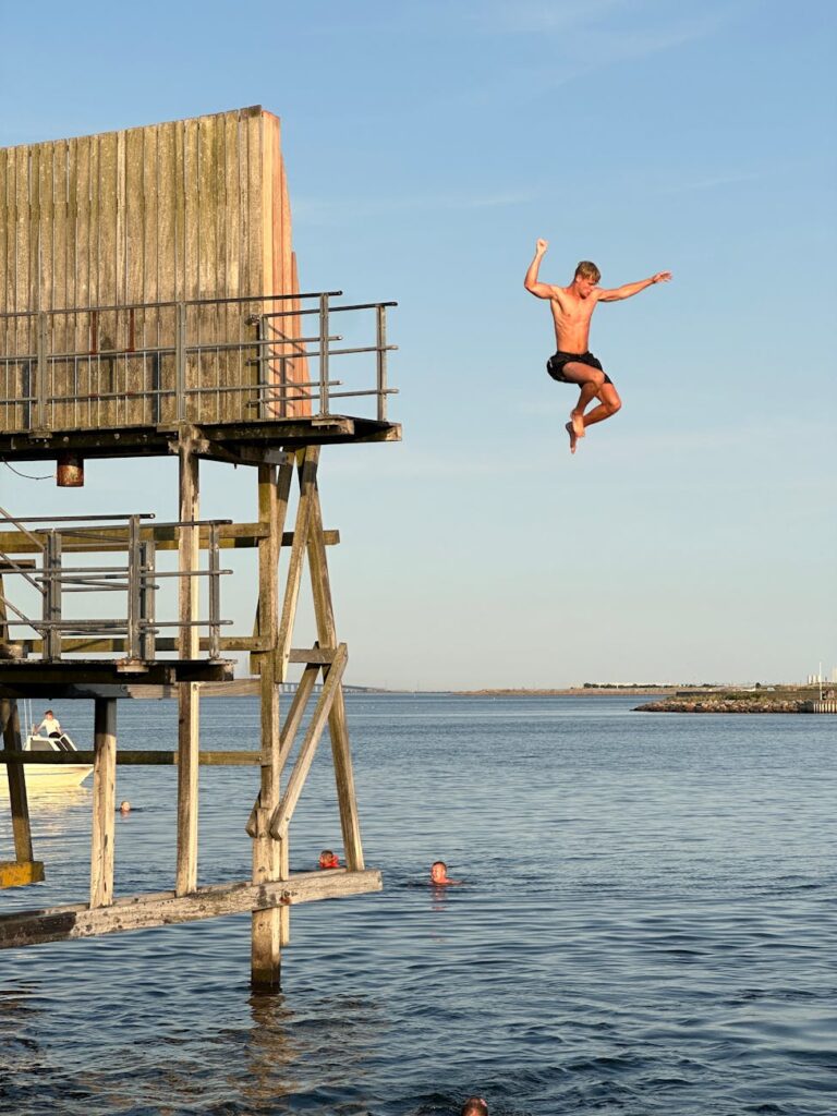 young man jumping into water from wooden boardwalk