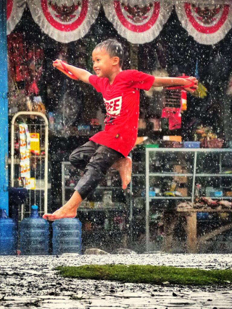 child jumping joyfully in rainy west java street