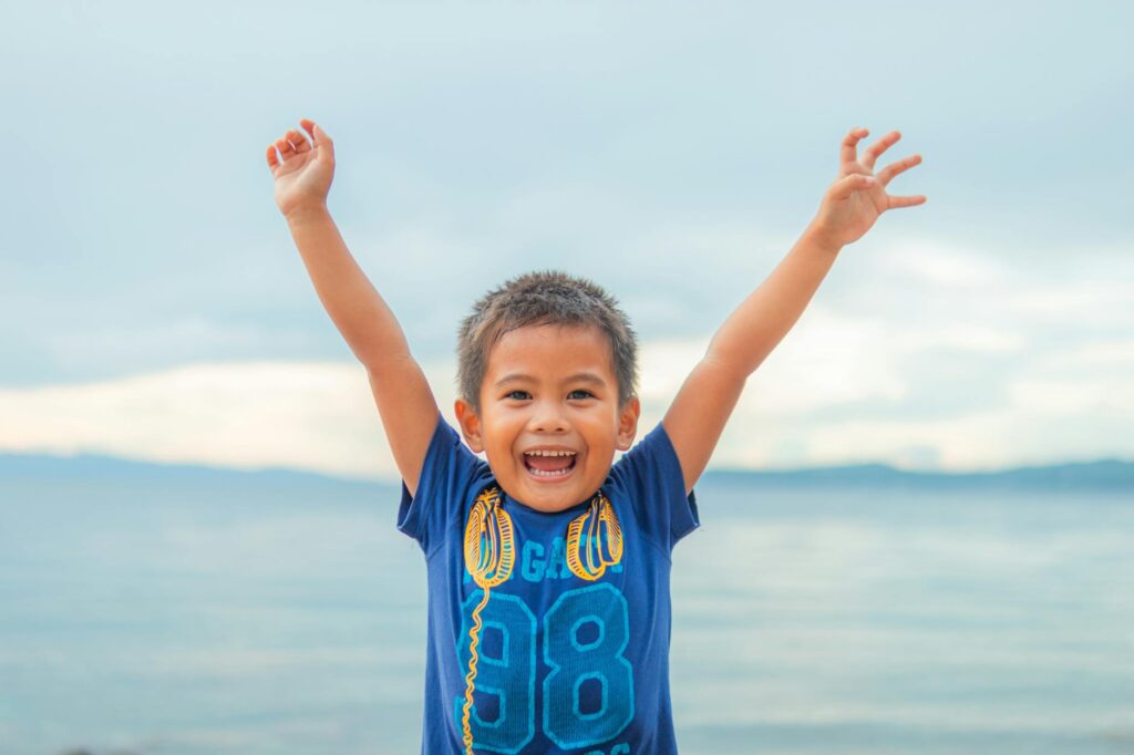 joyful young boy with arms raised outdoors