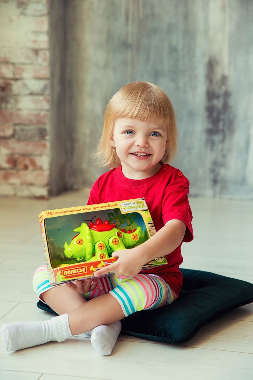 girl in red crew neck shirt holding a plastic toy animal