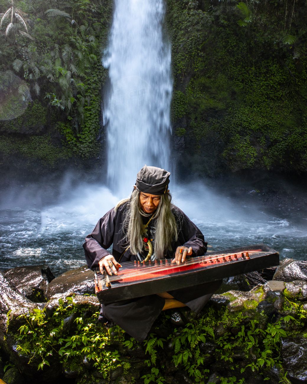 a woman playing an instrument near a waterfall